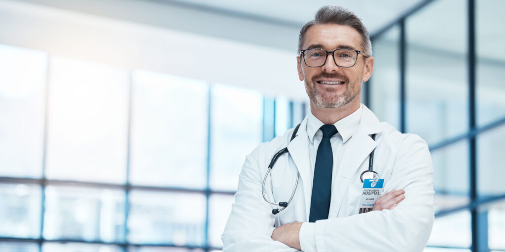 Doctor, man and happy with arms crossed in hospital for medical, career and happiness for portrait. medic, smile and work in clinic for healthcare, wellness and health while working in washington dc
