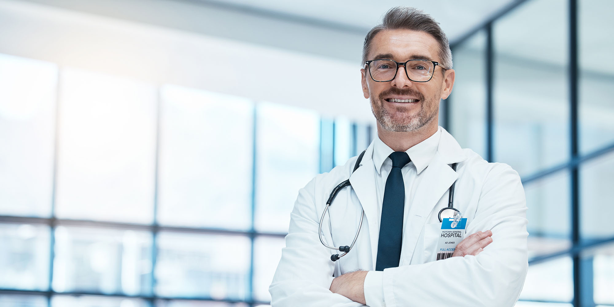 Doctor, man and happy with arms crossed in hospital for medical, career and happiness for portrait. medic, smile and work in clinic for healthcare, wellness and health while working in washington dc